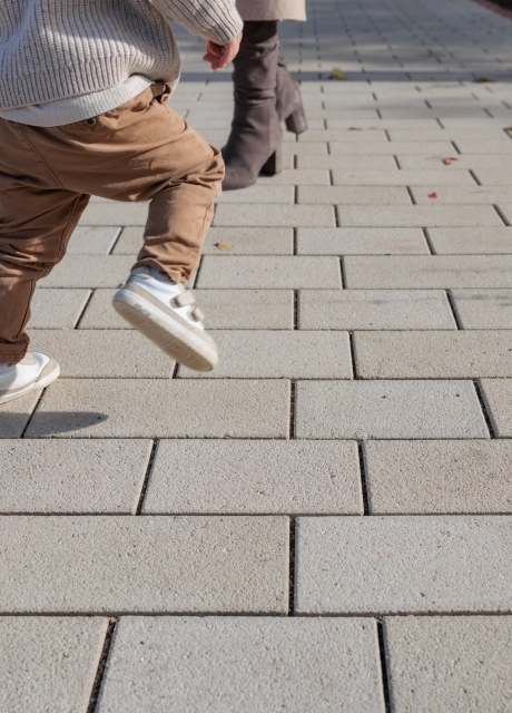 Close-up of a path made of beige GDM.KLIMASTEIN on which a child can be seen moving. Other people are standing along the path in the background.