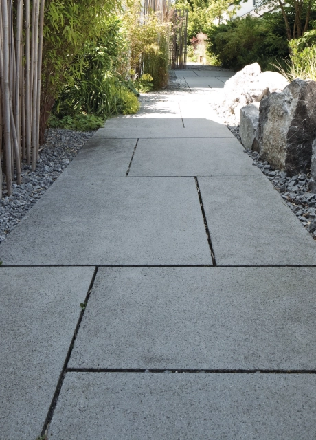 Gartenweg aus grauem Pflaster mit Splitt, Begrünung und Bambusstäben am Rand