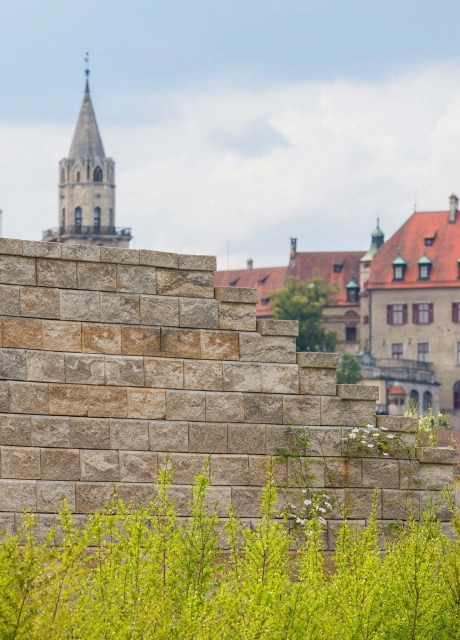 hohe sandfarbene Steinmauer und Ausblick auf mehrstöckiges braunes Gebäude und Kirchturm