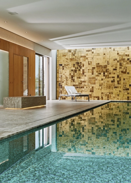 Großer Indoor-Pool vor einer Wand aus Gold- und Bronzefarbenen Wandfliesen