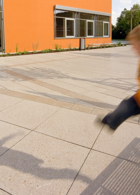 Kind auf mit Platten ausgelegtem Schulplatz vor Schulgebäude