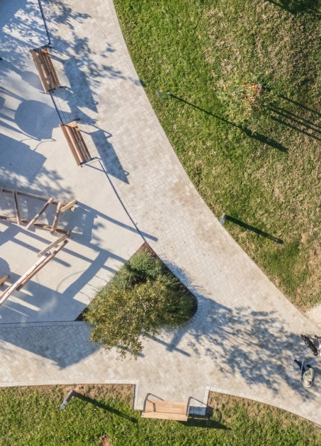 Aerial view of a modern playground area with light-coloured paths made of beige GDM.KLIMASTEIN, surrounded by green areas, benches and wooden play equipment.