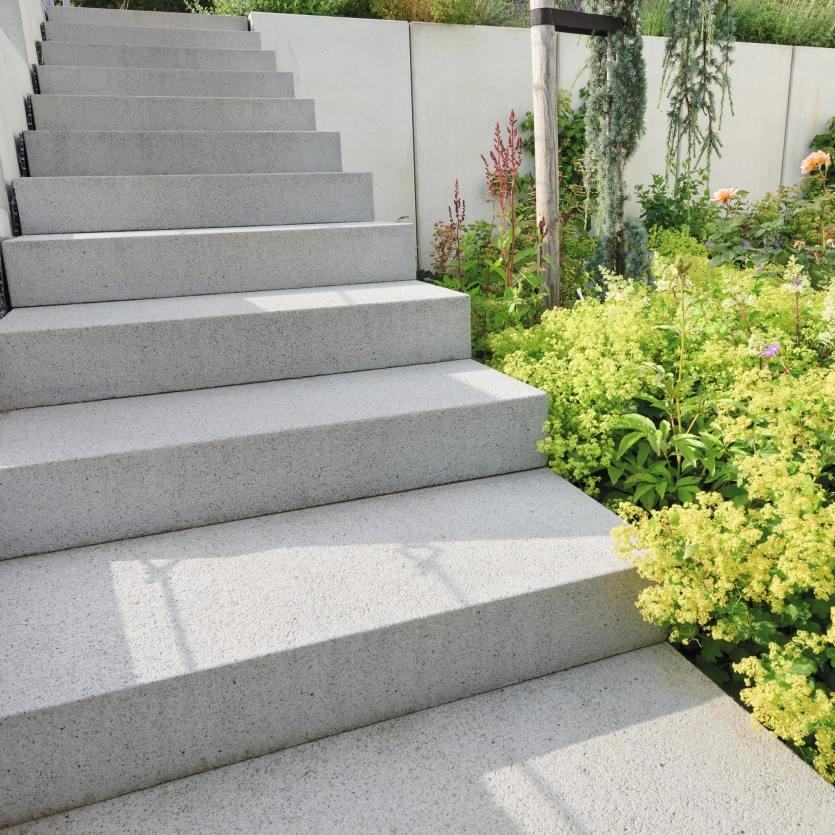 Stairs made of large, light-colored concrete steps that lead to a garden area planted with colorful flowers, grasses and shrubs.