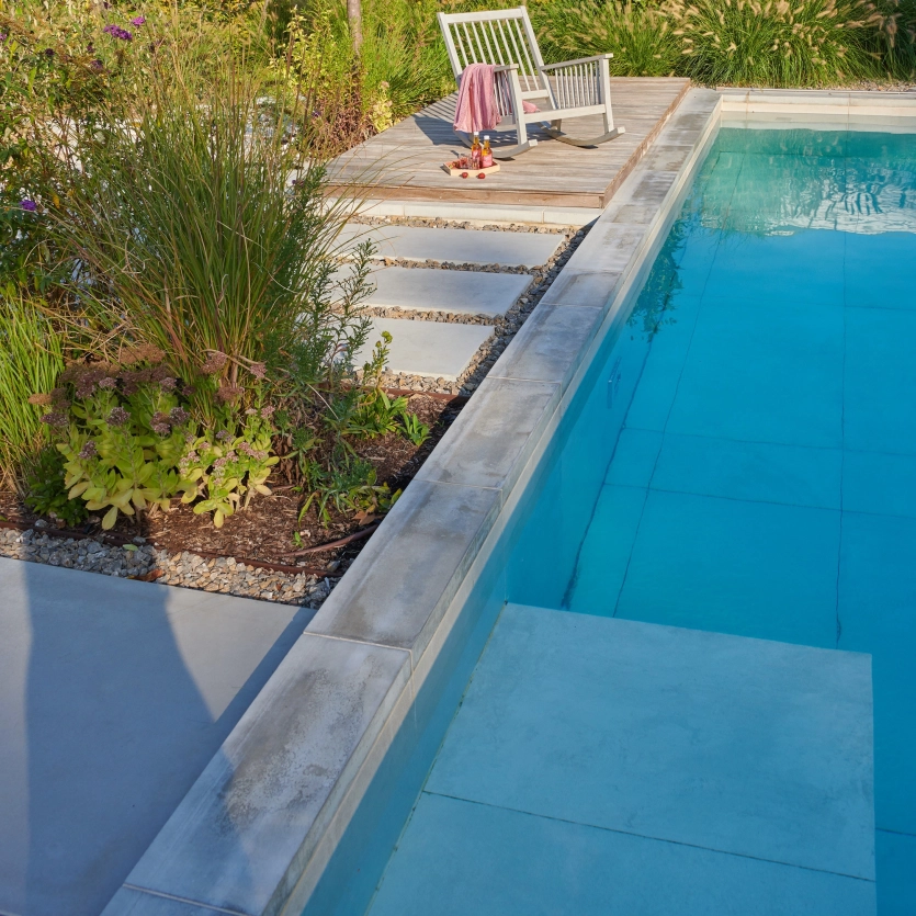 A cozy garden setting by the pool: a rocking chair surrounded by greenery invites you to enjoy the evening at the edge of the pool. The decking is equipped with GDM.MASSIMO.