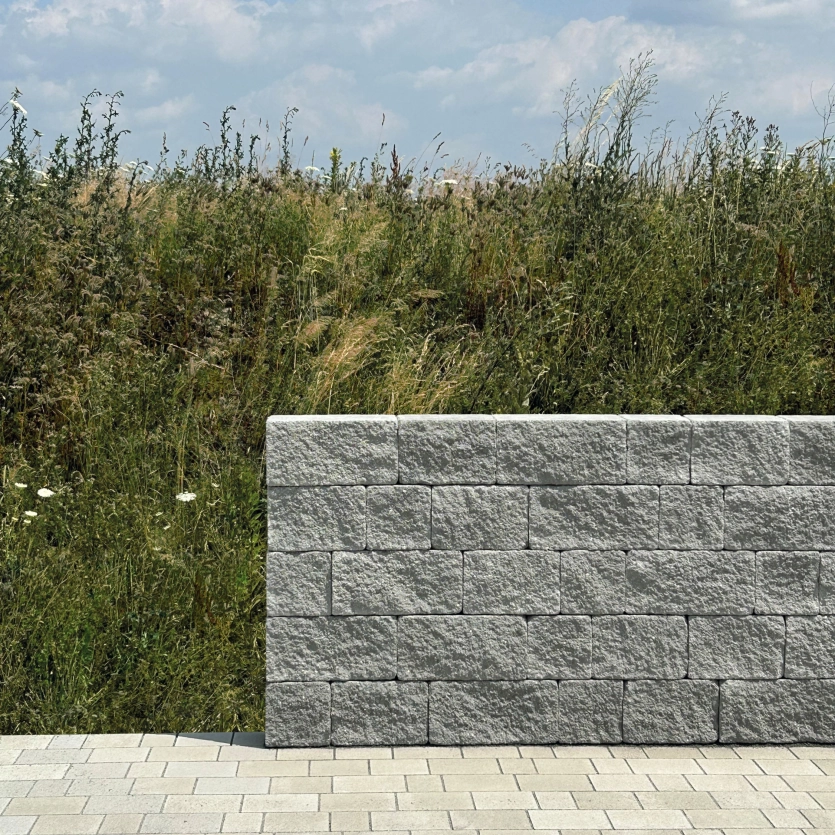 Gray privacy screen in front of a green slope under a blue sky.