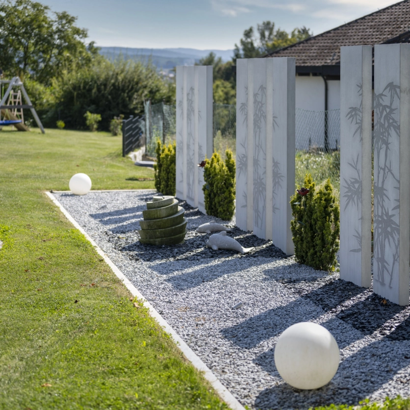 Nine steles made of high-performance concrete and blasted motifs as a privacy screen in a landscaped garden. 