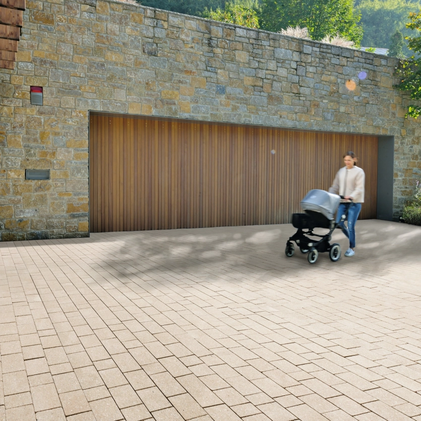A woman with a baby carriage on a driveway in front of a house with stone cladding