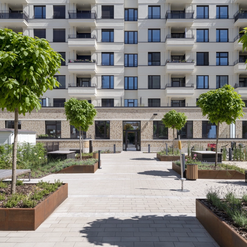 Vorplatz mit sandgrauen Pflastersteinen im Kleinformat und angrenzenden Cortenstahl Planzbeeten vor einer Wohnanlage