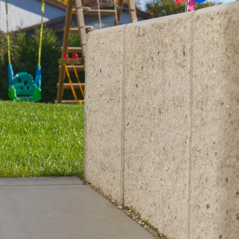 privater Garten mit Mauer aus L-Steinen und Schaukel für Kinder im Hintergrund