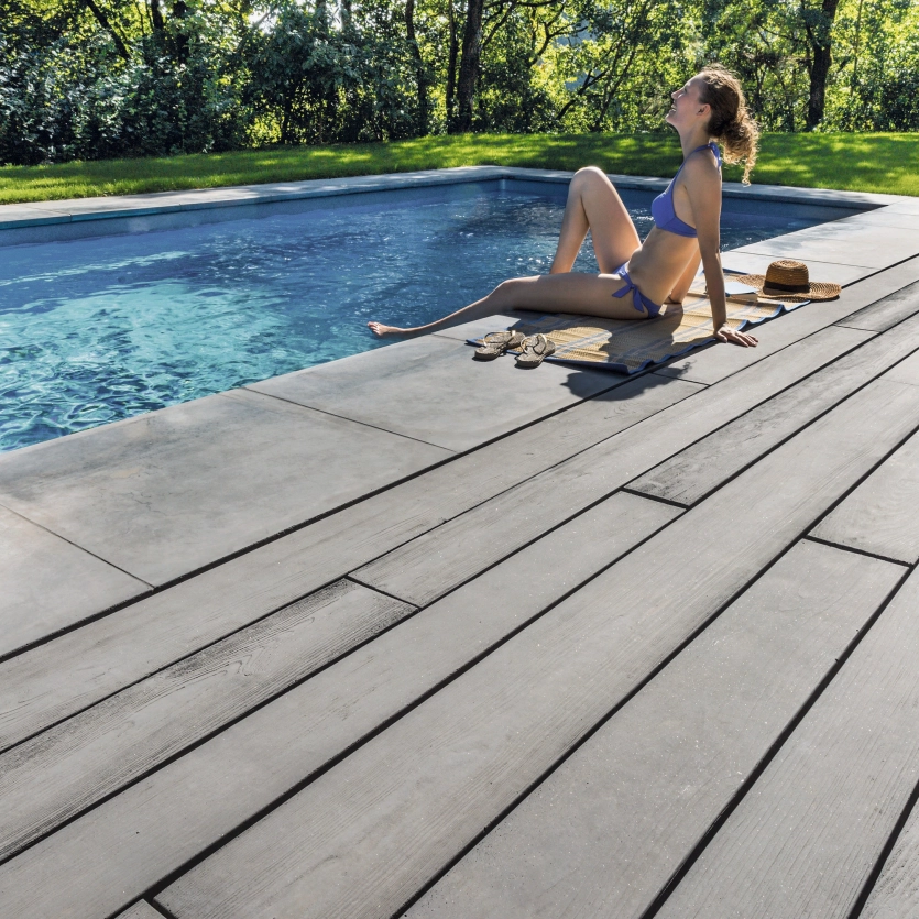 Woman sitting at the edge of the pool and enjoying the sun. The terrace is enlivened with wood-effect concrete planks from GODELMANN - GDM.MASSIMO plank.