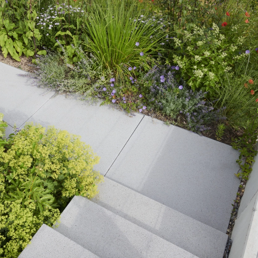 Stairs made of large, light-colored concrete slabs leading to a garden area planted with colorful flowers, grasses and shrubs.