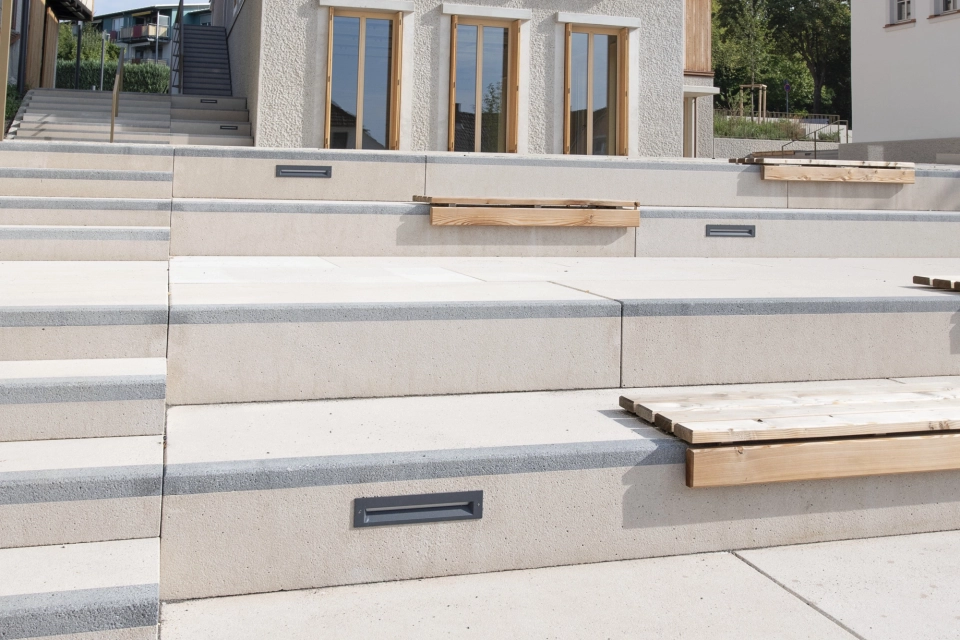 Modern and traditional buildings side by side, with an outdoor seating area in front of them in the style of an amphitheatre.