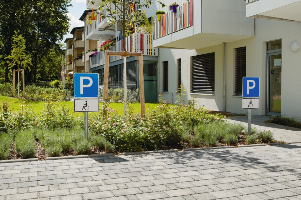 ausgewiesene Parkplätze vor 4-stöckigem weißen Wohngebäude mit Bankett