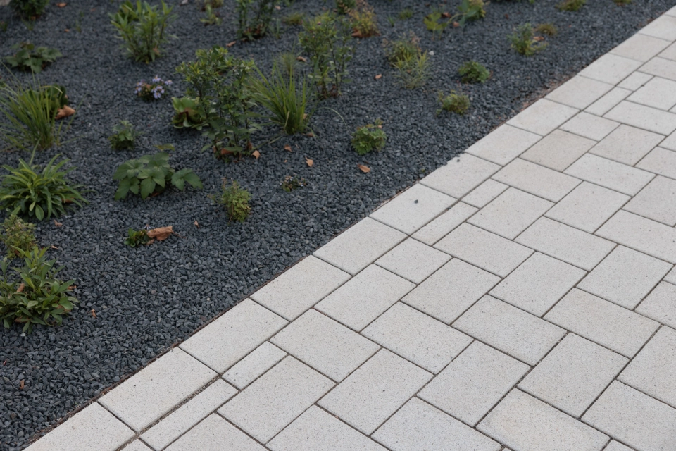 Close-up of a path made of beige GDM.KLIMASTEIN, bordering a planted bed with dark grit and young green plants.