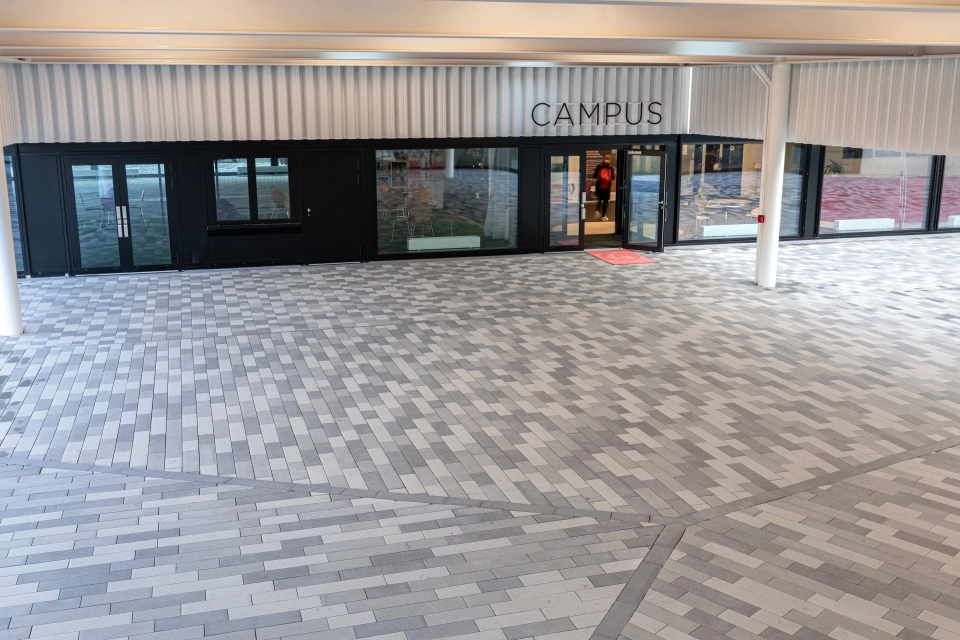 Überdachter Eingang zu modernem Sportzentrum mit Pflasterung in unterschiedlichen Grautönen