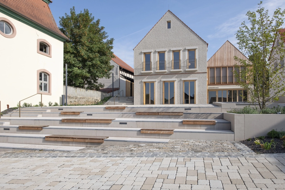 Modern and traditional buildings next to each other, with an outdoor seating area in front in the style of an amphitheatre.