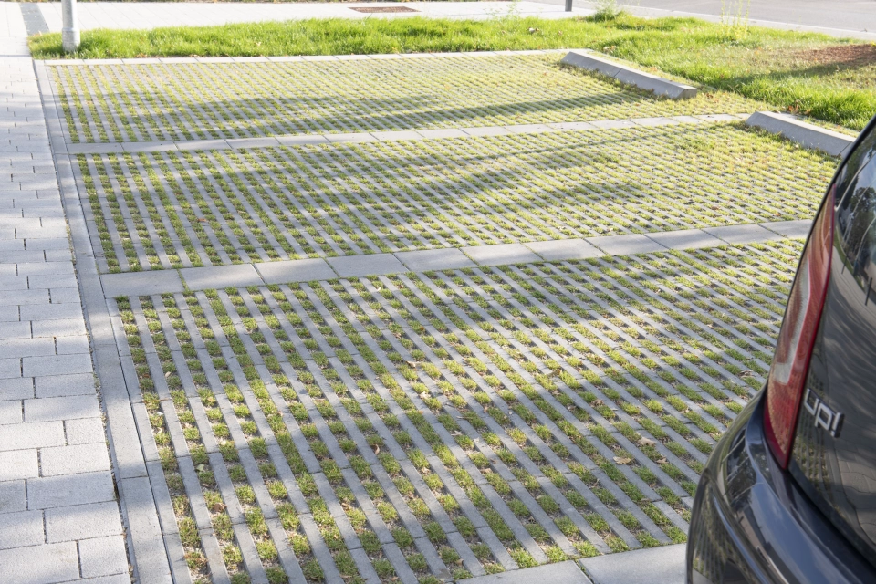 Close-up of a car park made of green grass paving stones. The individual parking spaces are separated by concrete blocks. Part of a black car can be seen in the foreground.