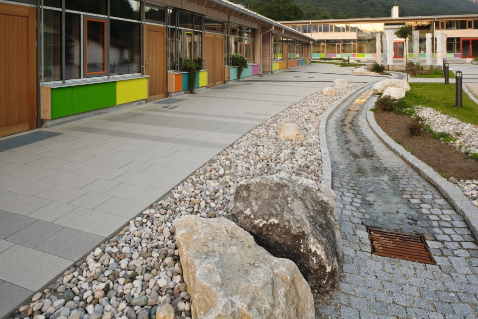 breiter gepflasterter Weg seitlich neben Gebäude mit bunten Fenstern und angelegtem Wasserlauf