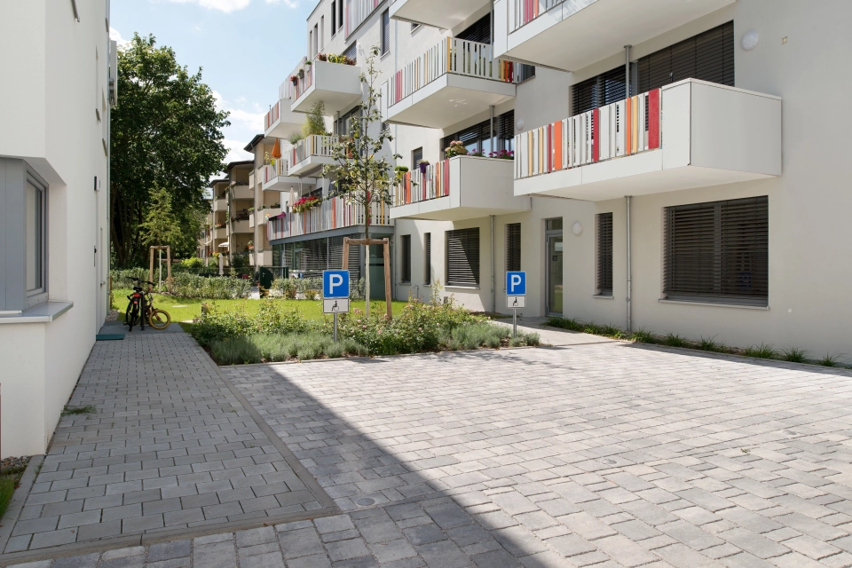 ausgewiesene Parkplätze vor 4-stöckigem weißen Wohngebäude mit Bankett