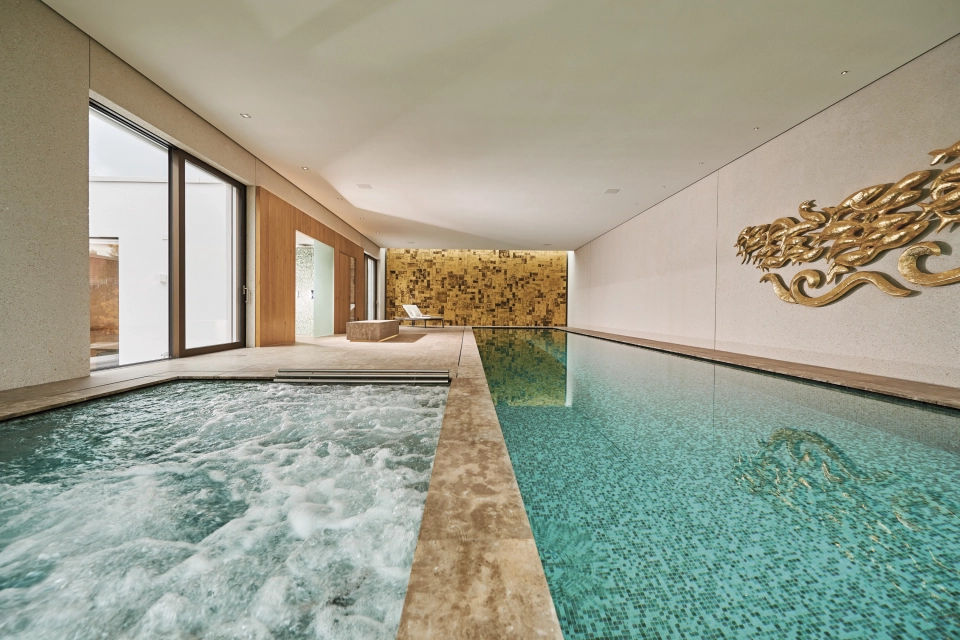 Großer Indoor-Pool vor einer Wand aus Gold- und Bronzefarbenen Wandfliesen